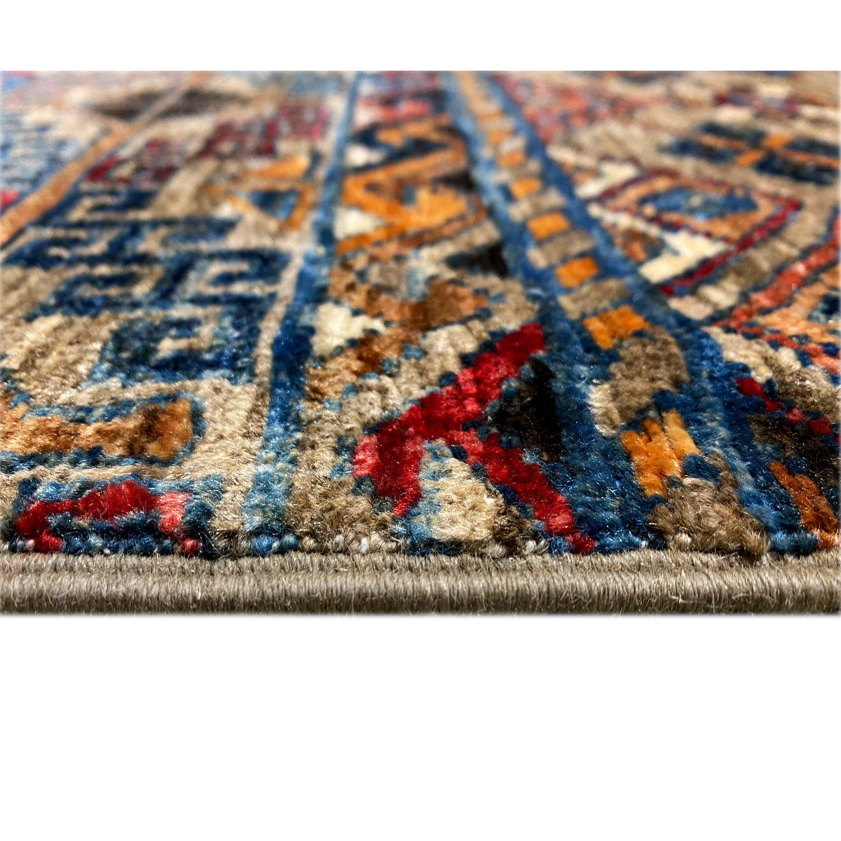 Nahaufnahme Teppichoberfläche mit farbigen Ornamenten und dichter Florstruktur, sichtbarer Saum.