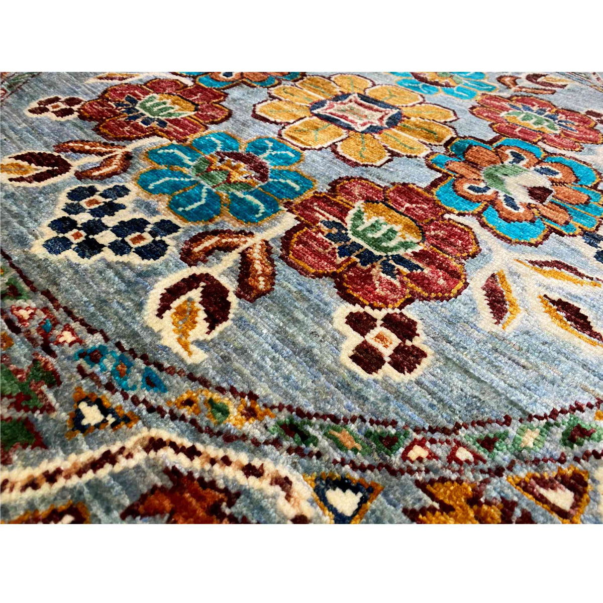 Detailansicht Wollteppich: bunte Blumenmotive auf blauem Grund mit Stickereioptik