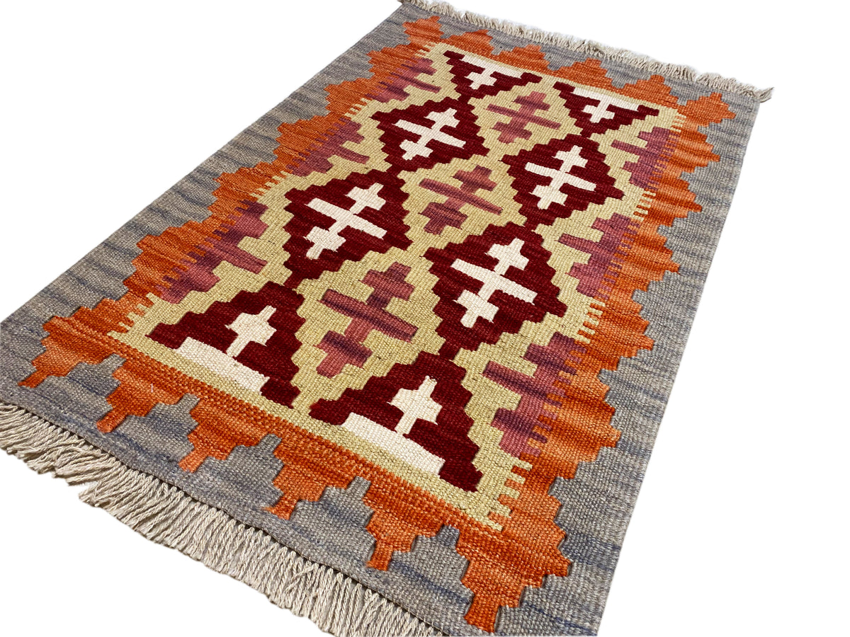 Kelim-Teppich schräg: grafisches Ornamentmuster in Orange, Creme und Dunkelrot auf Grau