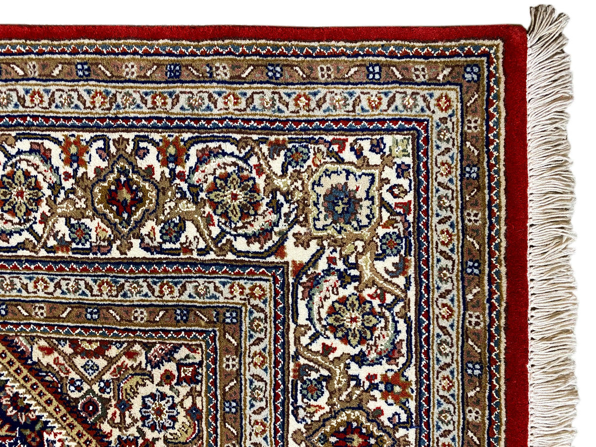 Teppich mit roter Grundfläche, weiß-blauen Ornamenten und seitlicher Fransenborte