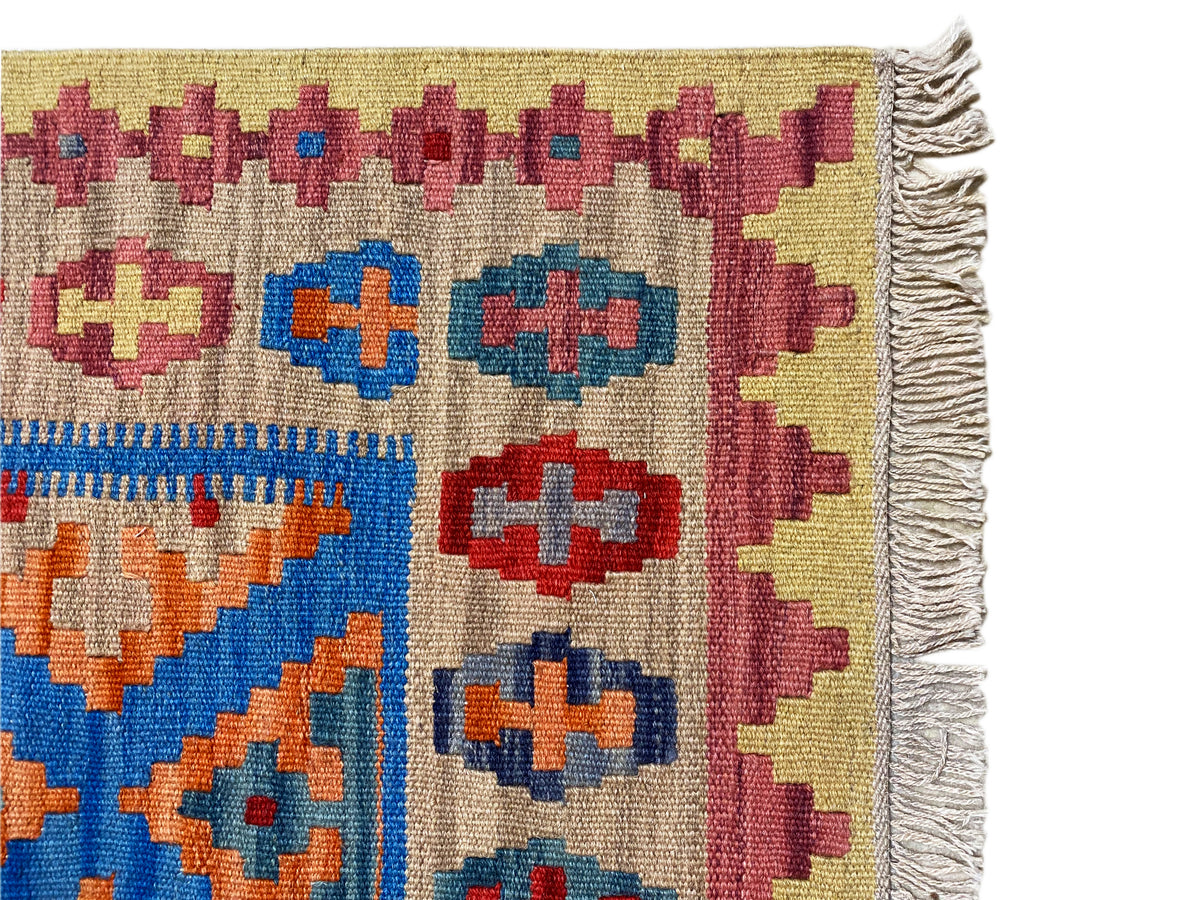 Kelim-Teppich Detail mit gedrehten Fransen rechts und buntem geometrischem Muster auf beigem Grund