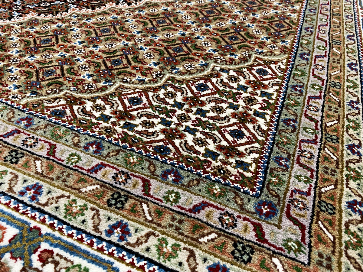 Ecke eines braunen Indo-Tabriz Teppichs mit bunten Ornamenten, Zierborte und Fransen.