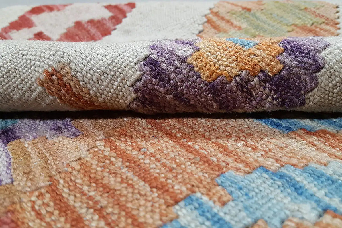 Kelim-Teppich Detail: grob gewebte Textur mit lila, orangefarbenen und blauen Mustern
