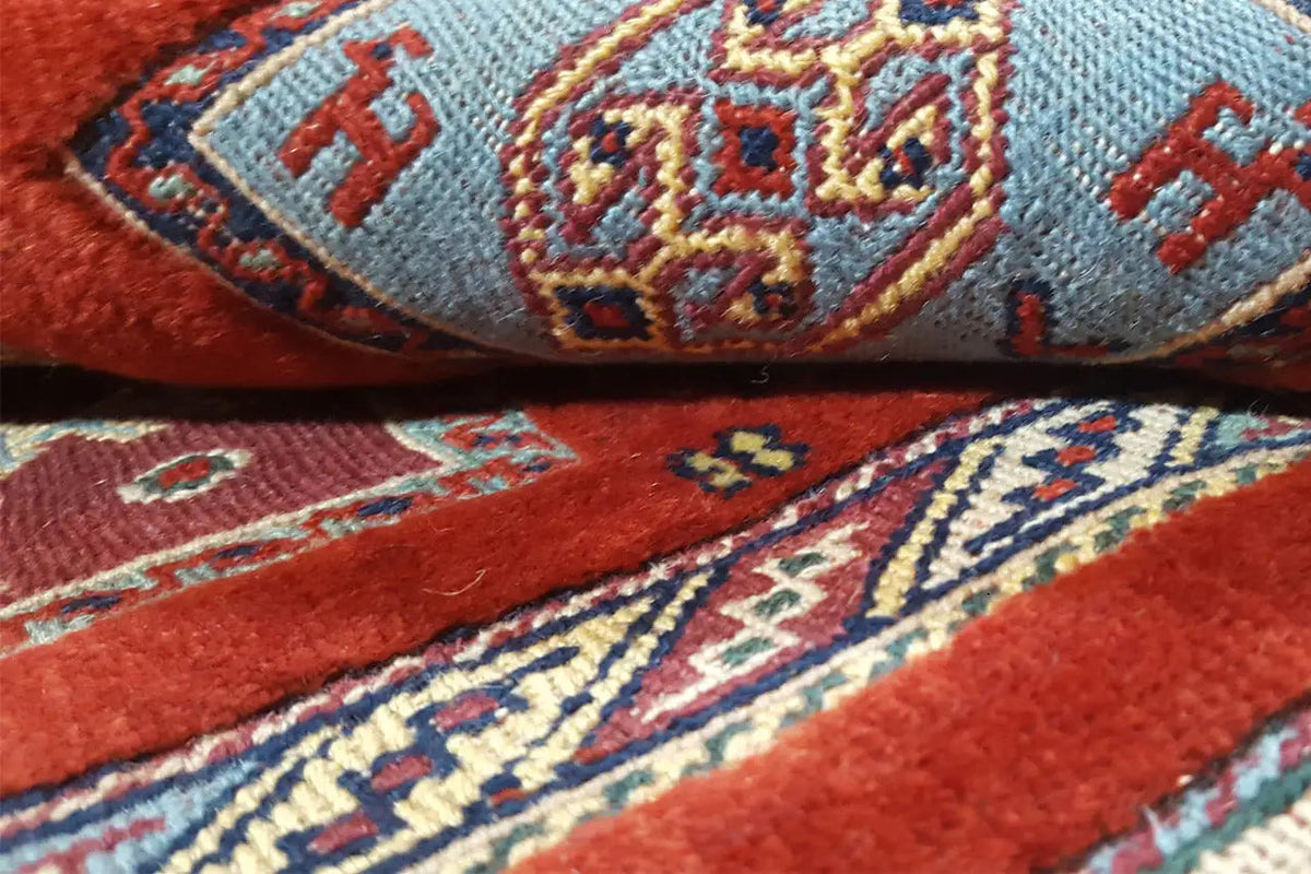 Detail eines Orientteppichs: rotes Feld, blaue und gelbe Ornamente, Webstruktur