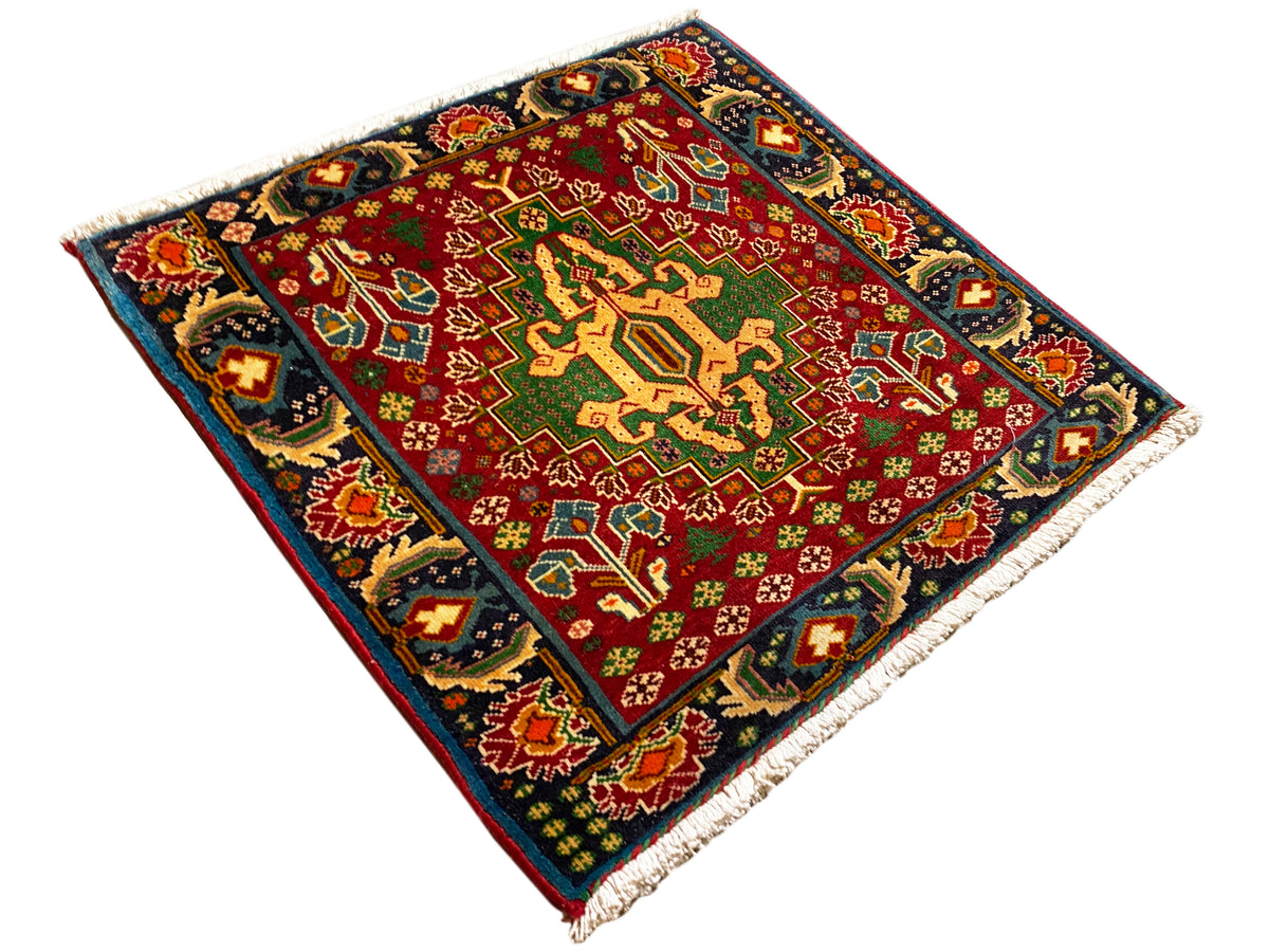 Rechteckiger Teppich (67x66 cm) diagonal fotografiert; rotes Feld, dunkle Einfassung, Fransen