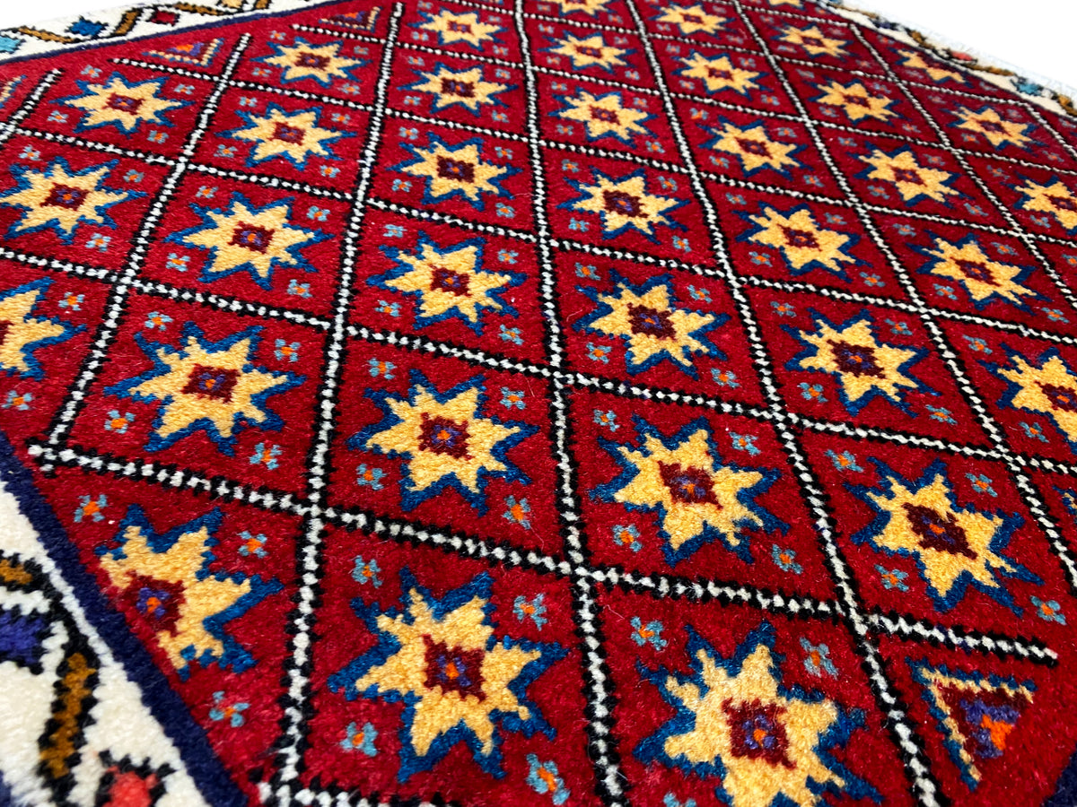 Nahaufnahme vom Teppich: rotes Rautenfeld mit gelben und blauen Sternen